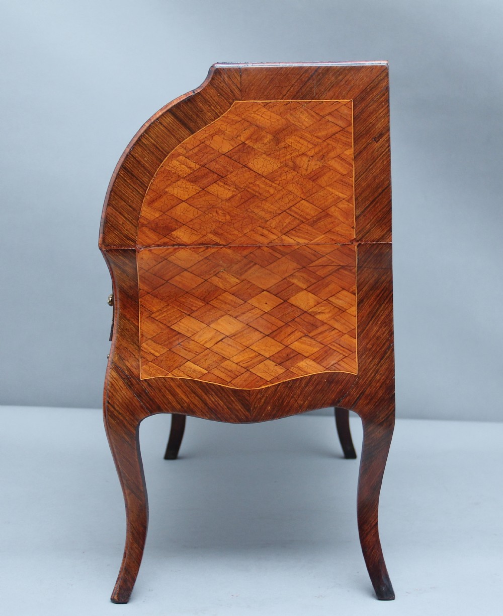 A 19th-century miniature walnut desk with geometric parquetry pattern, a cylinder roll top, cabriole legs, and brass handles. View VII