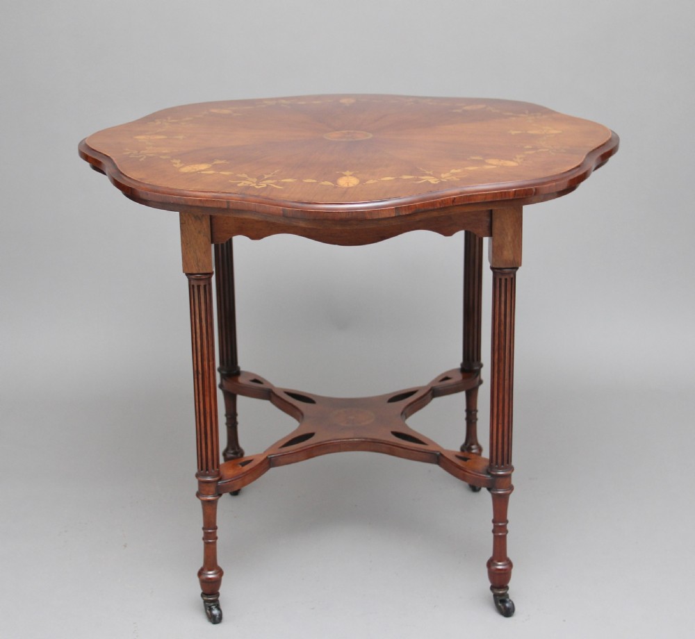 A 19th-century rosewood centre table with a serpentine-edged marquetry top, four fluted legs, an X-shaped stretcher, and brass castors.