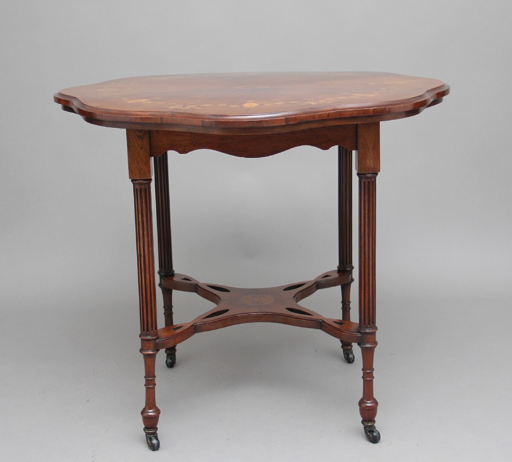 A 19th-century rosewood centre table with a serpentine-edged marquetry top, four fluted legs, an X-shaped stretcher, and brass castors. View II