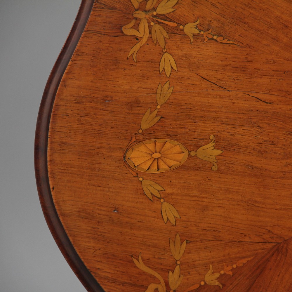 A 19th-century rosewood centre table with a serpentine-edged marquetry top, four fluted legs, an X-shaped stretcher, and brass castors. View IV