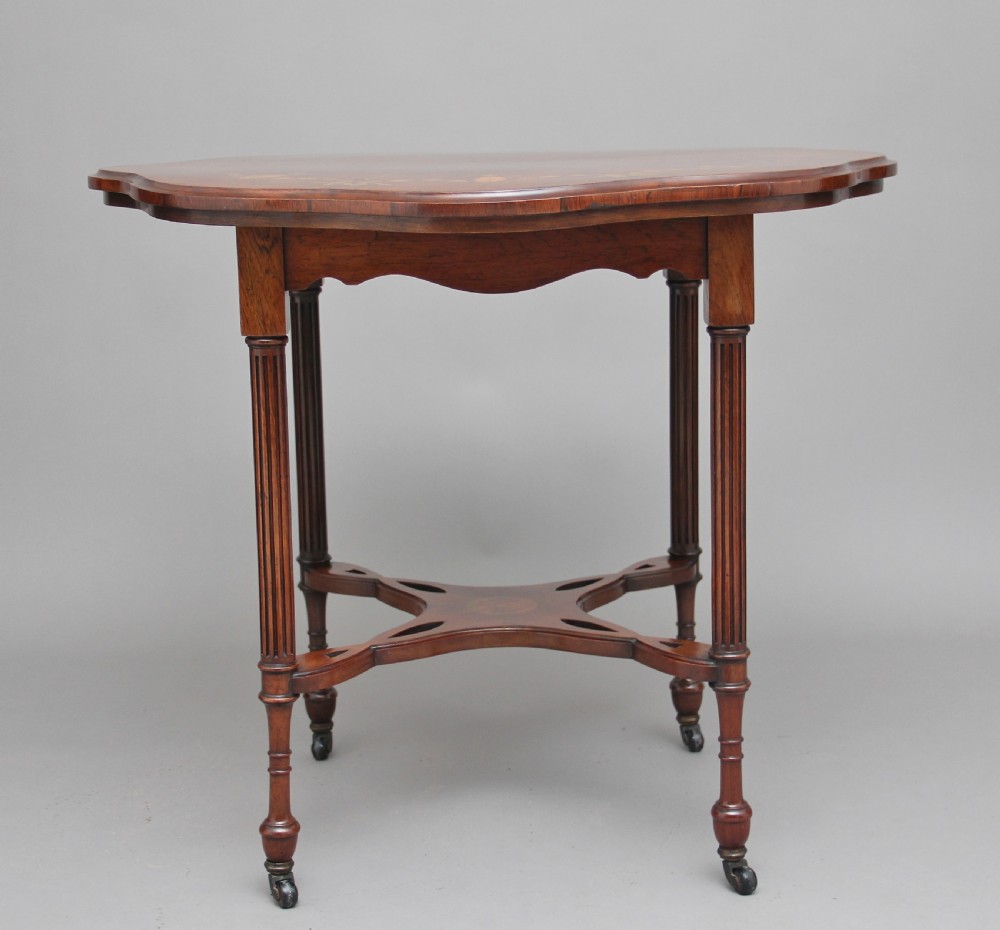 A 19th-century rosewood centre table with a serpentine-edged marquetry top, four fluted legs, an X-shaped stretcher, and brass castors. View V