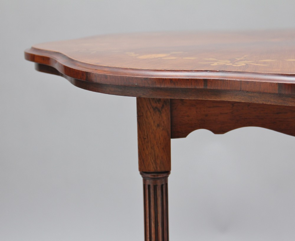 A 19th-century rosewood centre table with a serpentine-edged marquetry top, four fluted legs, an X-shaped stretcher, and brass castors. View IX