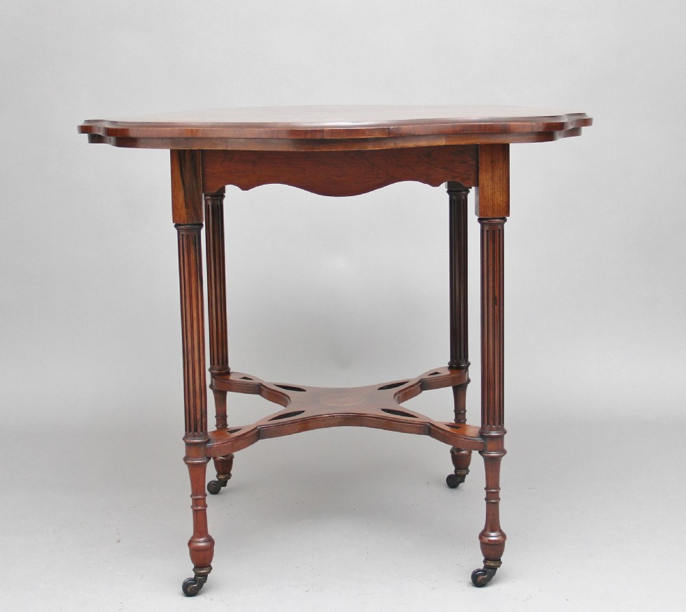 A 19th-century rosewood centre table with a serpentine-edged marquetry top, four fluted legs, an X-shaped stretcher, and brass castors. View XI