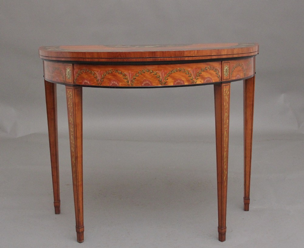 An early nineteenth-century demilune satinwood card table featuring hand-painted floral swags along the apron and slender tapered square legs.