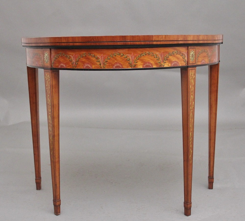 An early nineteenth-century demilune satinwood card table featuring hand-painted floral swags along the apron and slender tapered square legs. View II