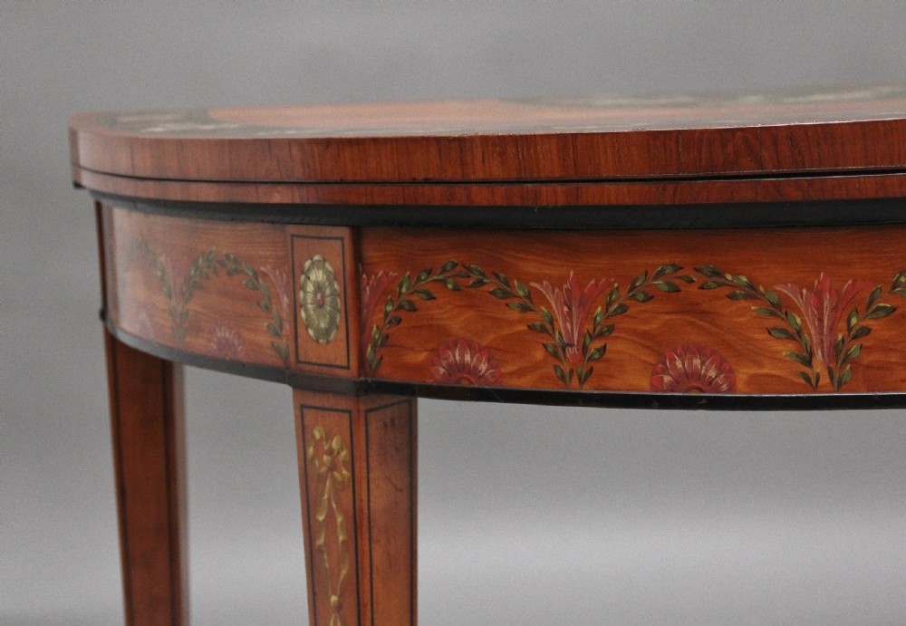 An early nineteenth-century demilune satinwood card table featuring hand-painted floral swags along the apron and slender tapered square legs. View III