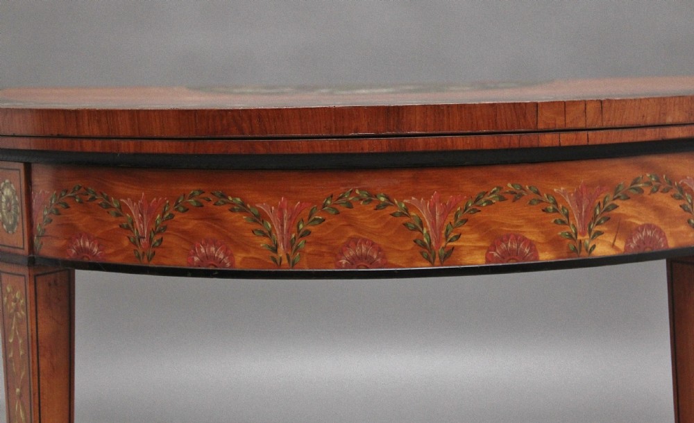 An early nineteenth-century demilune satinwood card table featuring hand-painted floral swags along the apron and slender tapered square legs. View IV