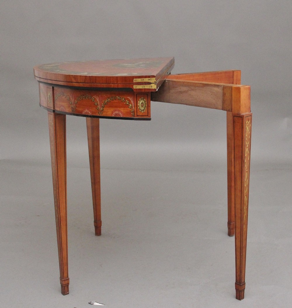 An early nineteenth-century demilune satinwood card table featuring hand-painted floral swags along the apron and slender tapered square legs. View VIII