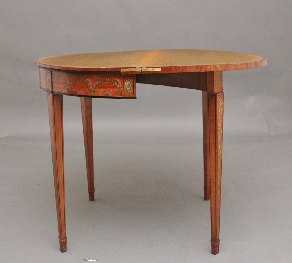 An early nineteenth-century demilune satinwood card table featuring hand-painted floral swags along the apron and slender tapered square legs. View IX