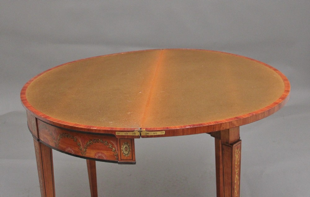 An early nineteenth-century demilune satinwood card table featuring hand-painted floral swags along the apron and slender tapered square legs. View X