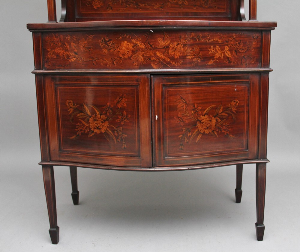 A 19th-century mahogany display cabinet featuring floral marquetry inlays, a glazed upper section with glass shelves, and a bow-front lower cabinet on tapered legs. View IX