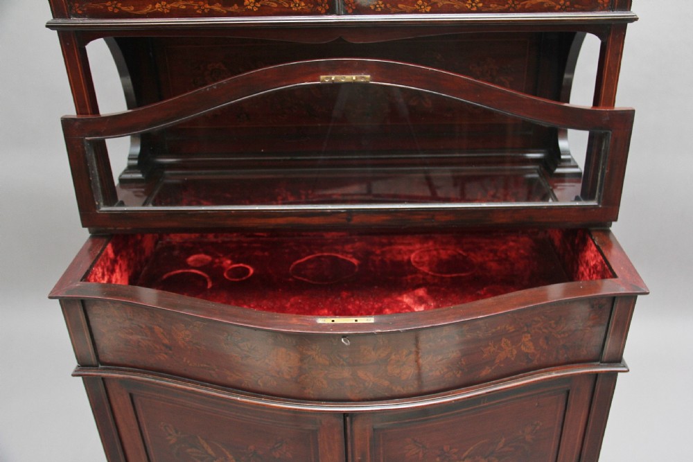 A 19th-century mahogany display cabinet featuring floral marquetry inlays, a glazed upper section with glass shelves, and a bow-front lower cabinet on tapered legs. View XI
