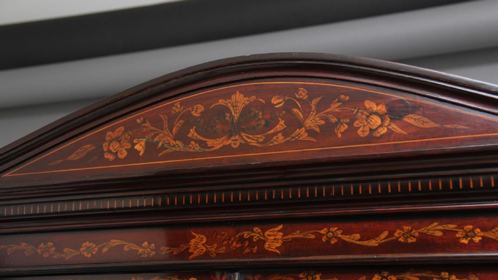 A 19th-century mahogany display cabinet featuring floral marquetry inlays, a glazed upper section with glass shelves, and a bow-front lower cabinet on tapered legs. View XV