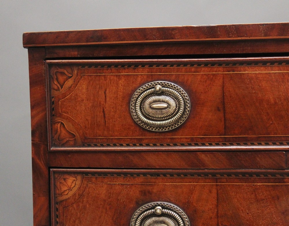An 18th-century bowfront mahogany chest featuring four graduated drawers with oval brass ring handles, decorative inlay, and splayed bracket feet. View II