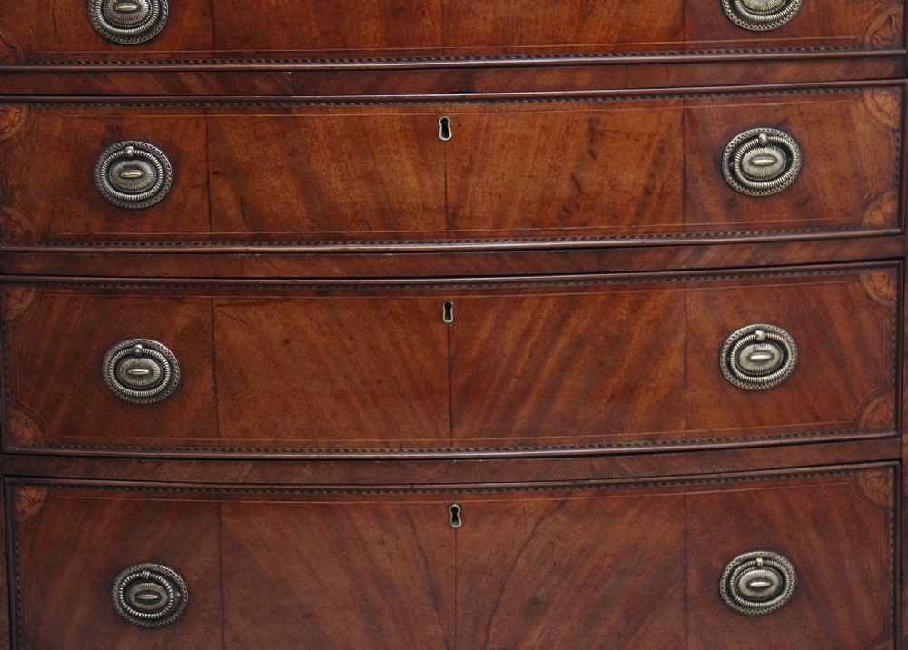 An 18th-century bowfront mahogany chest featuring four graduated drawers with oval brass ring handles, decorative inlay, and splayed bracket feet. View III