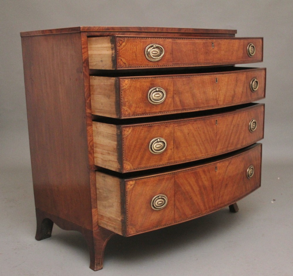 An 18th-century bowfront mahogany chest featuring four graduated drawers with oval brass ring handles, decorative inlay, and splayed bracket feet. View V