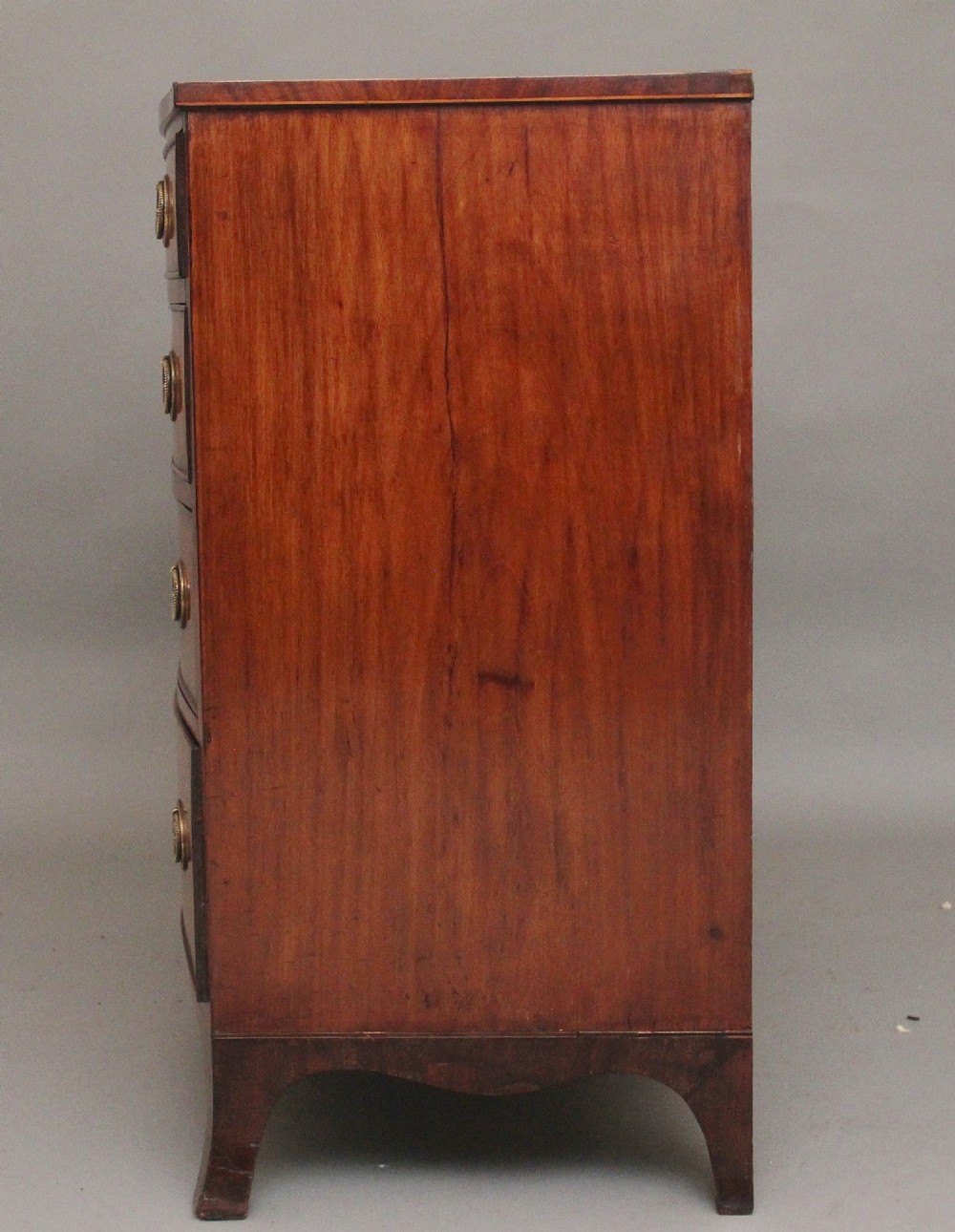 An 18th-century bowfront mahogany chest featuring four graduated drawers with oval brass ring handles, decorative inlay, and splayed bracket feet. View IX
