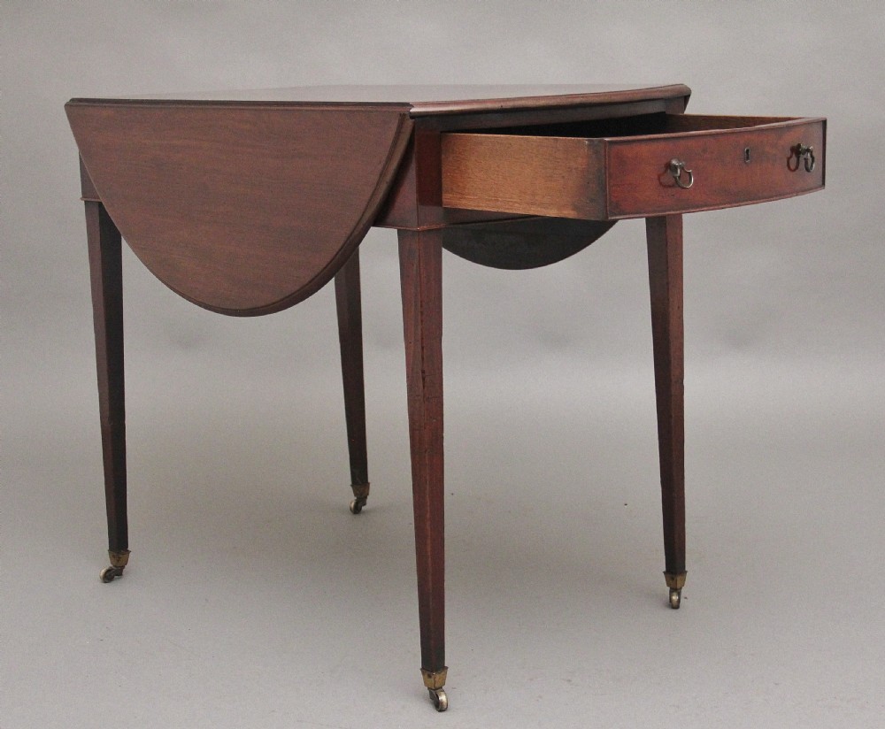 An 18th-century mahogany Pembroke table featuring drop-down curved side leaves, a front drawer with ring pull handles, and square tapered legs on brass castors. View II