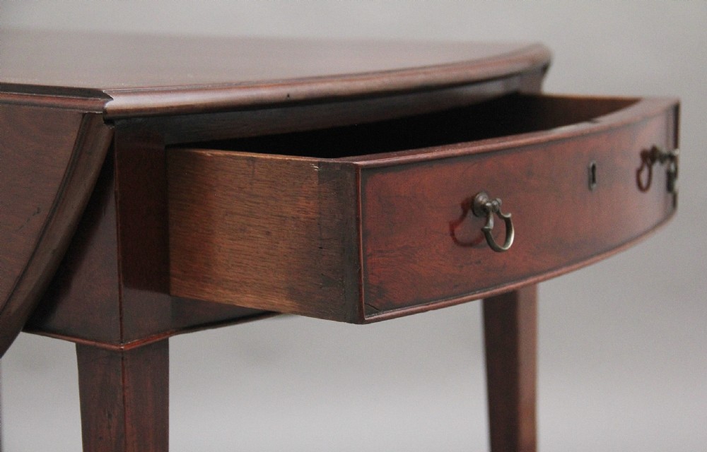 An 18th-century mahogany Pembroke table featuring drop-down curved side leaves, a front drawer with ring pull handles, and square tapered legs on brass castors. View III
