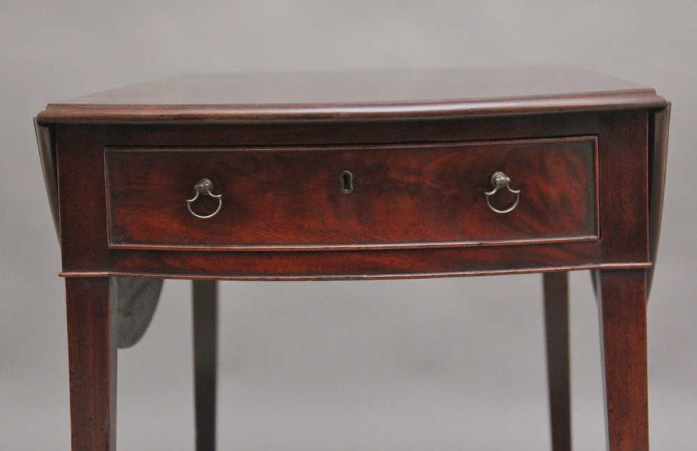 An 18th-century mahogany Pembroke table featuring drop-down curved side leaves, a front drawer with ring pull handles, and square tapered legs on brass castors. View V