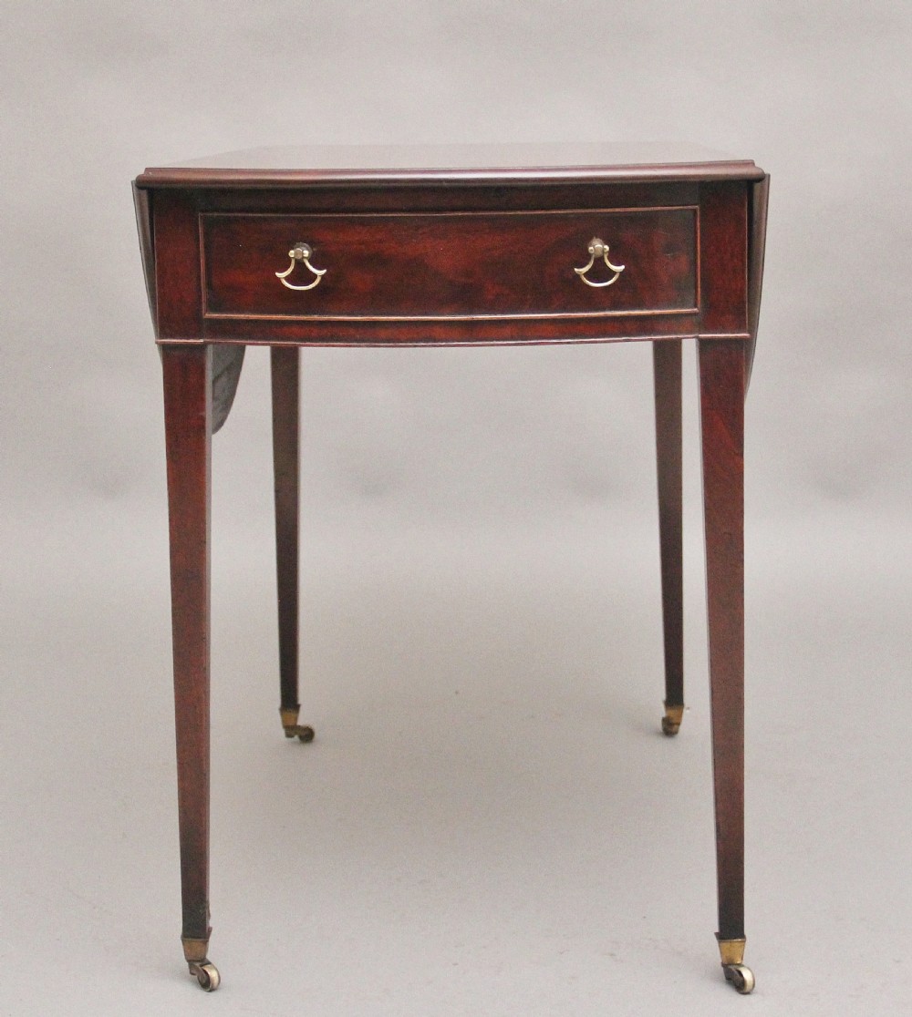 An 18th-century mahogany Pembroke table featuring drop-down curved side leaves, a front drawer with ring pull handles, and square tapered legs on brass castors. View VII