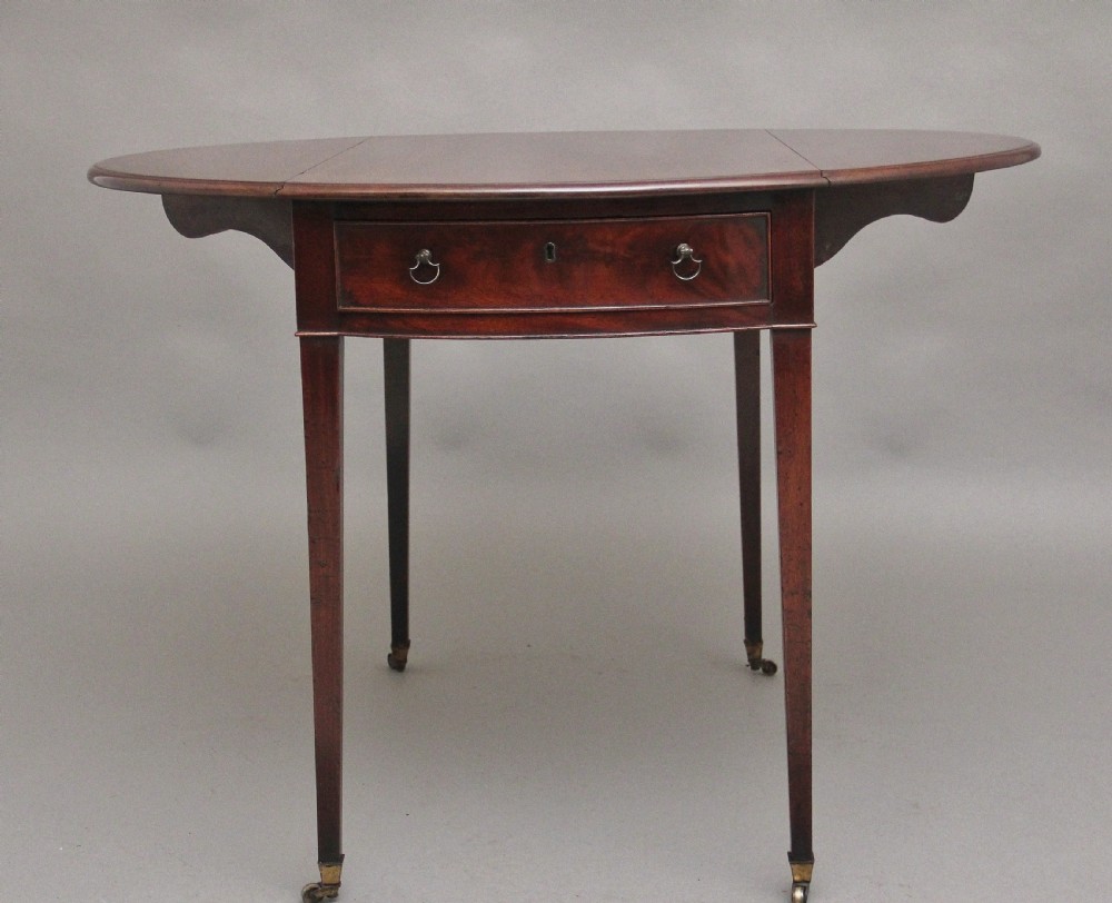 An 18th-century mahogany Pembroke table featuring drop-down curved side leaves, a front drawer with ring pull handles, and square tapered legs on brass castors. View VIII