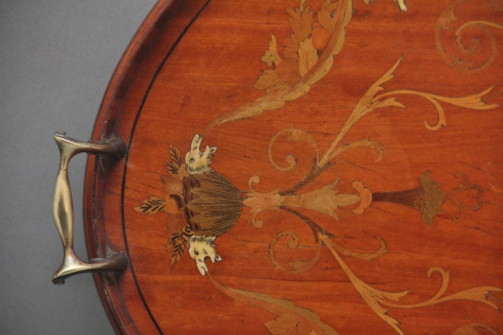 An oval 19th-century satinwood tray featuring detailed marquetry inlays of cherubs, foliate scrolls, a central sunburst medallion, and brass handles at each end. View IV