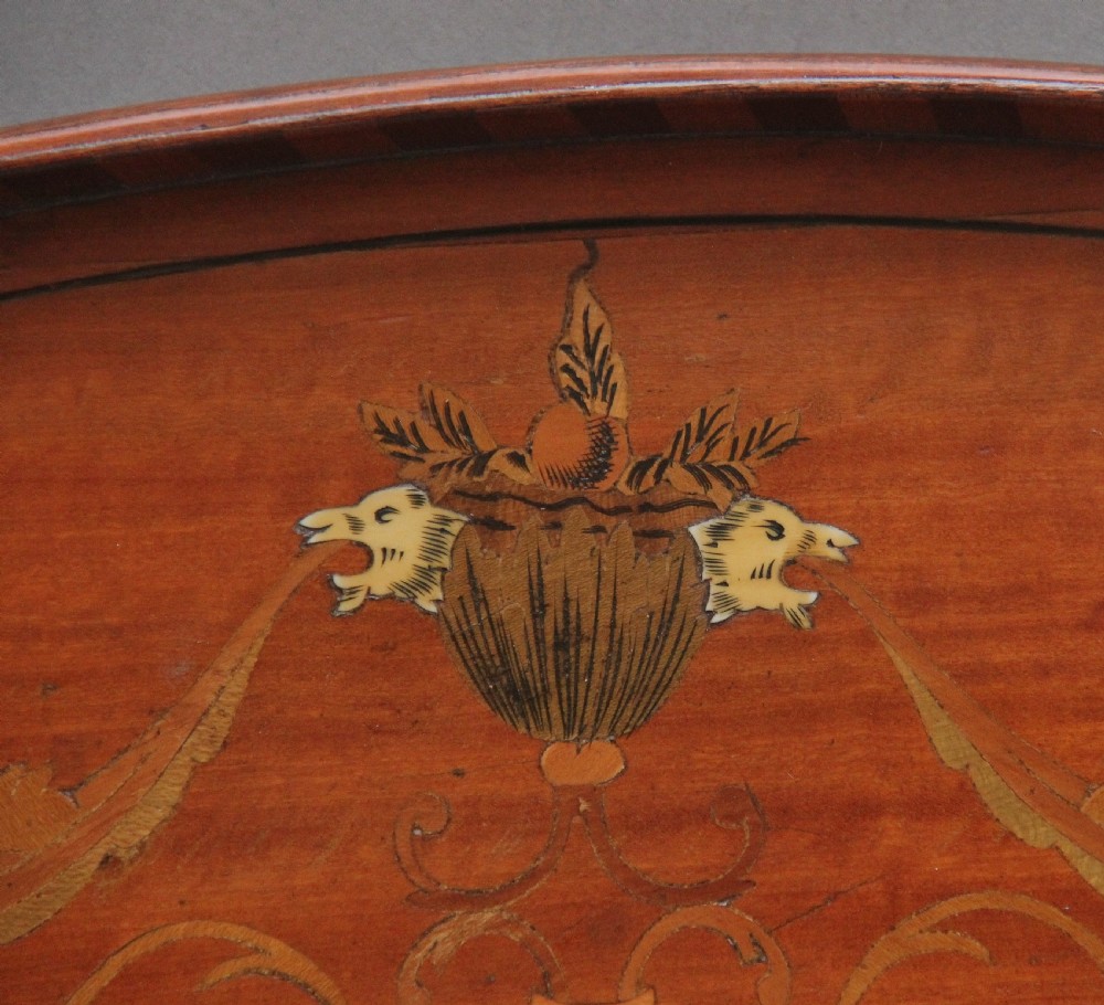 An oval 19th-century satinwood tray featuring detailed marquetry inlays of cherubs, foliate scrolls, a central sunburst medallion, and brass handles at each end. View VI