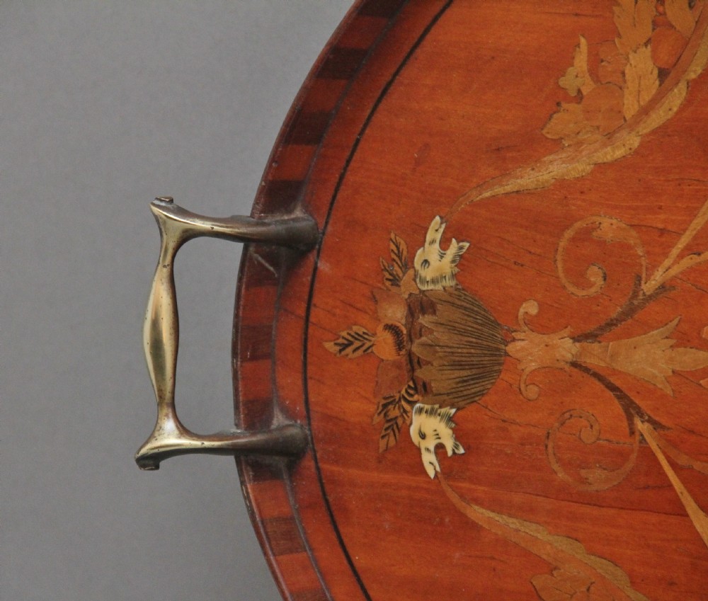 An oval 19th-century satinwood tray featuring detailed marquetry inlays of cherubs, foliate scrolls, a central sunburst medallion, and brass handles at each end. View VIII