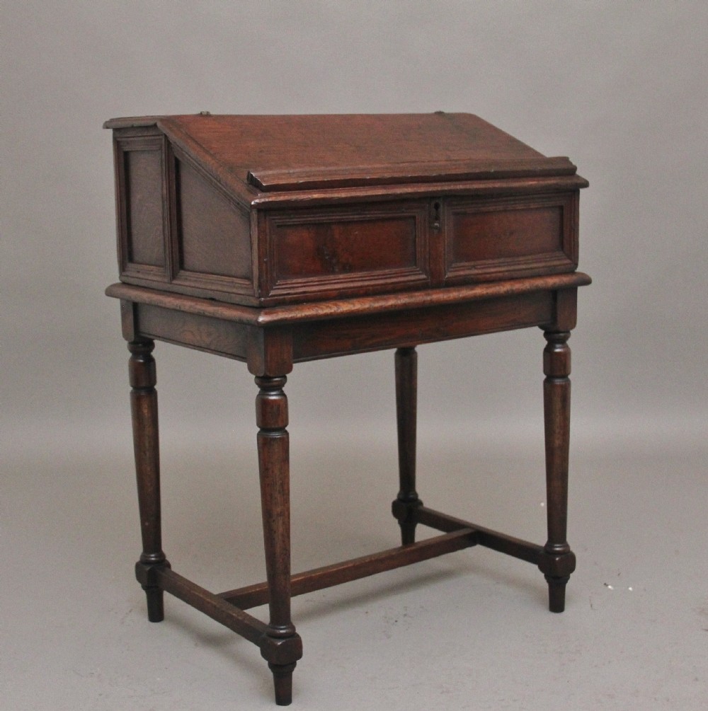 An 18th-century dark oak slope-front writing desk mounted on a stand with turned legs and lower stretchers.