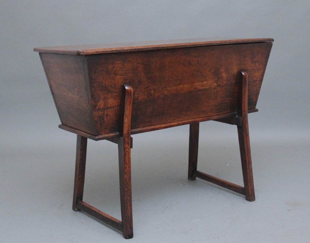 An 18th-century elm dough bin with a flat rectangular lid resting on a four-legged timber stand.