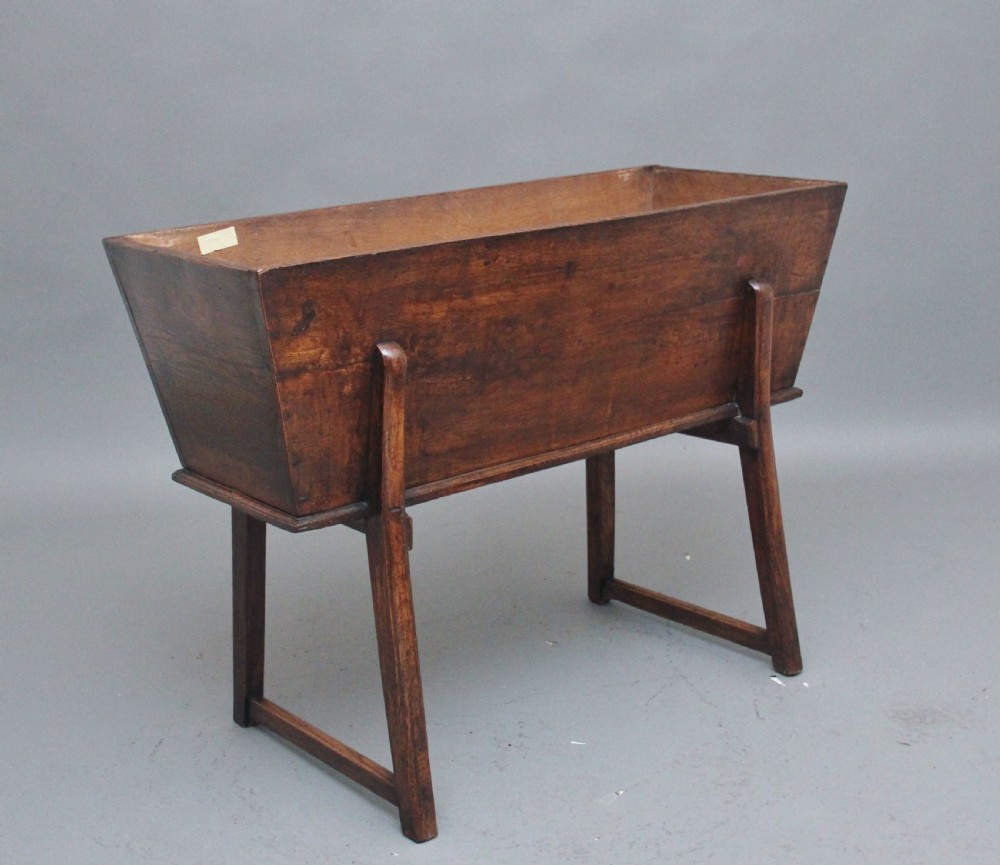 An 18th-century elm dough bin with a flat rectangular lid resting on a four-legged timber stand. View II