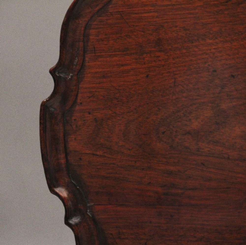 An 18th-century dark mahogany tripod table with a carved scalloped edge shown with its top tilted vertically on a turned pedestal stem. View VIII