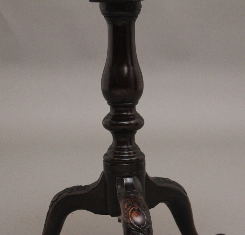 An 18th-century dark mahogany tripod table with a carved scalloped edge shown with its top tilted vertically on a turned pedestal stem. View X
