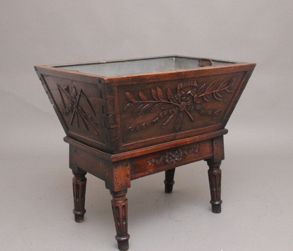 An 18th-century French carved walnut wine cooler featuring a zinc-lined tapered basin set on a stand with fluted legs and ribbon relief carvings.