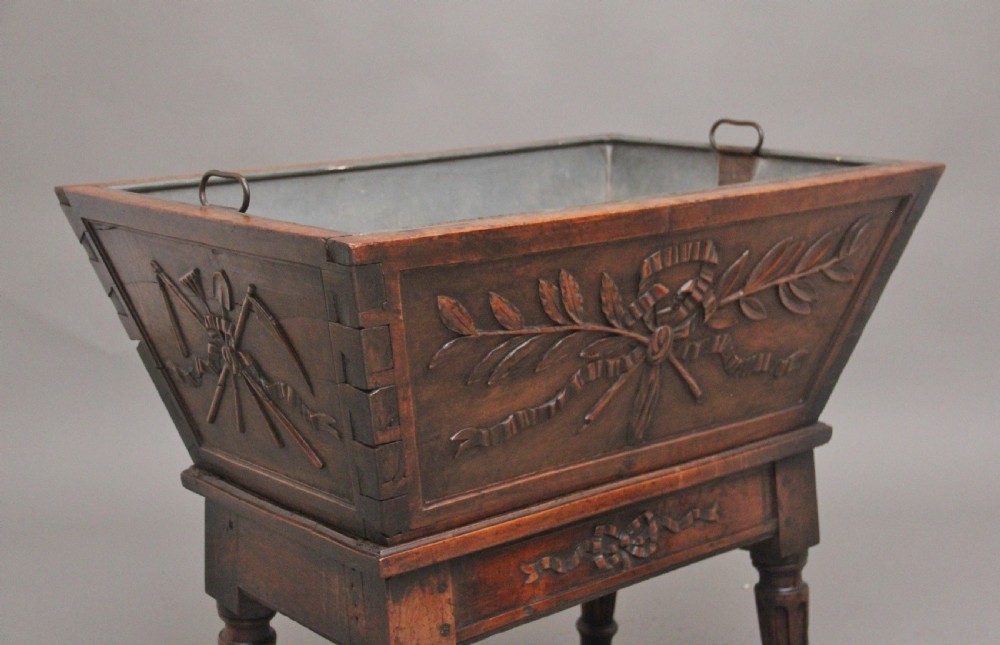 An 18th-century French carved walnut wine cooler featuring a zinc-lined tapered basin set on a stand with fluted legs and ribbon relief carvings. View II