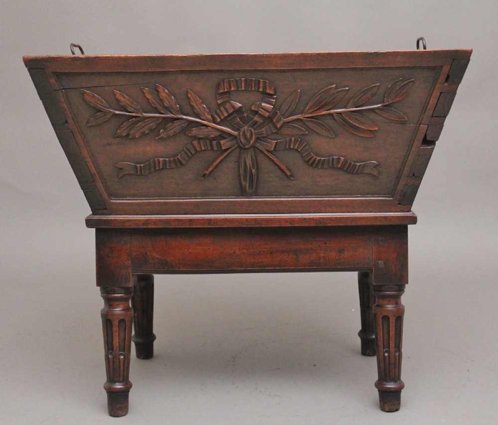 An 18th-century French carved walnut wine cooler featuring a zinc-lined tapered basin set on a stand with fluted legs and ribbon relief carvings. View X