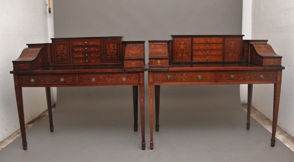 A pair of early 20th-century mahogany Carlton House desks with detailed satinwood marquetry inlay, stepped gallery drawers, and tapered legs. View IV
