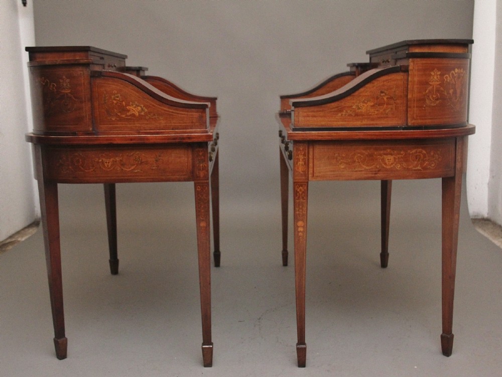 A pair of early 20th-century mahogany Carlton House desks with detailed satinwood marquetry inlay, stepped gallery drawers, and tapered legs. View V