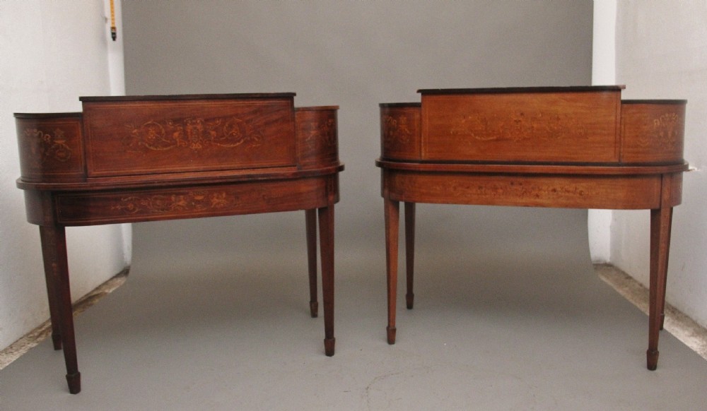 A pair of early 20th-century mahogany Carlton House desks with detailed satinwood marquetry inlay, stepped gallery drawers, and tapered legs. View VI