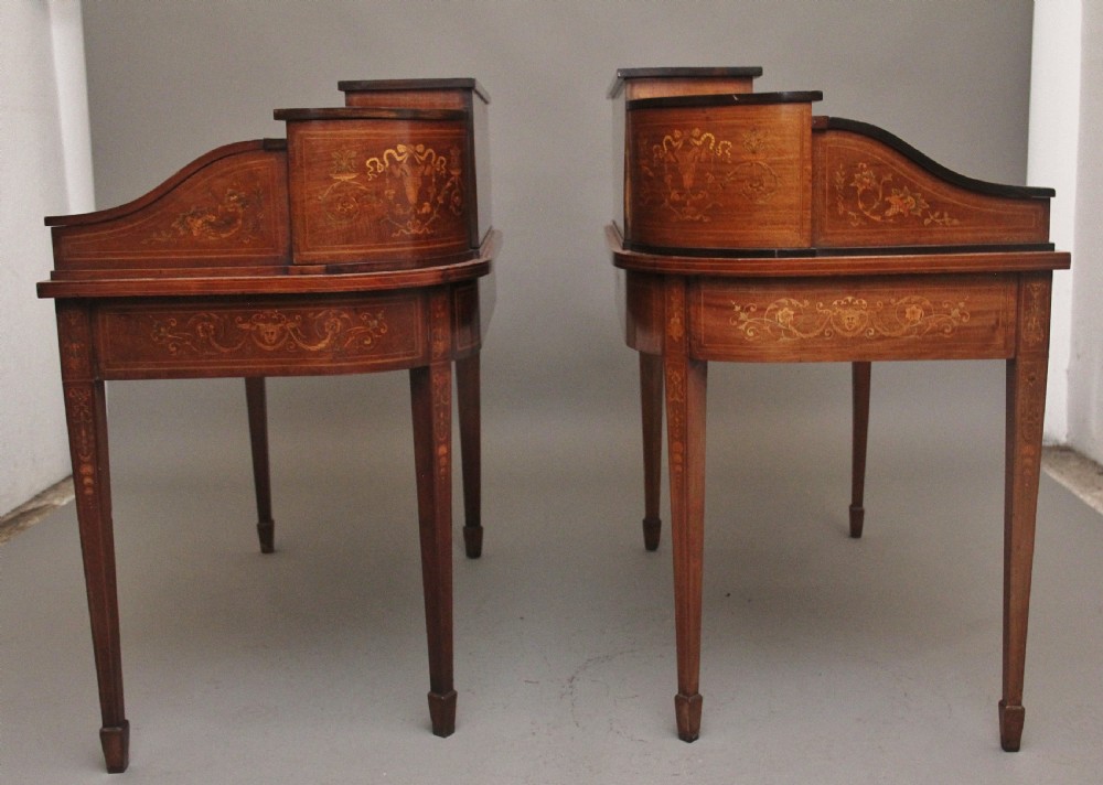 A pair of early 20th-century mahogany Carlton House desks with detailed satinwood marquetry inlay, stepped gallery drawers, and tapered legs. View VII