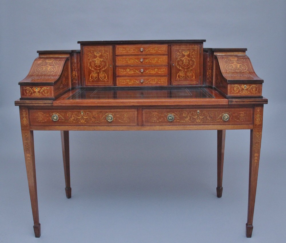 A pair of early 20th-century mahogany Carlton House desks with detailed satinwood marquetry inlay, stepped gallery drawers, and tapered legs. View VIII