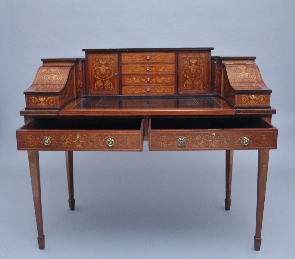 A pair of early 20th-century mahogany Carlton House desks with detailed satinwood marquetry inlay, stepped gallery drawers, and tapered legs. View IX