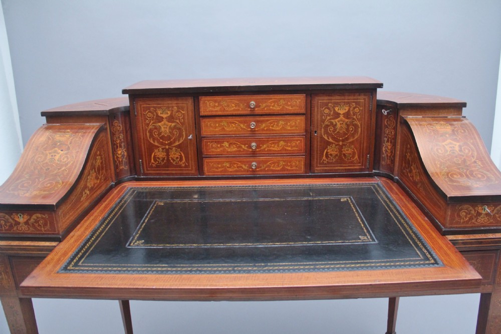 A pair of early 20th-century mahogany Carlton House desks with detailed satinwood marquetry inlay, stepped gallery drawers, and tapered legs. View X