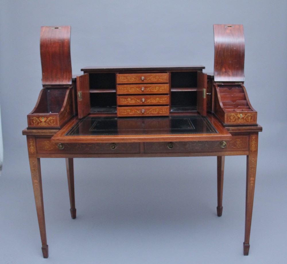 A pair of early 20th-century mahogany Carlton House desks with detailed satinwood marquetry inlay, stepped gallery drawers, and tapered legs. View XI