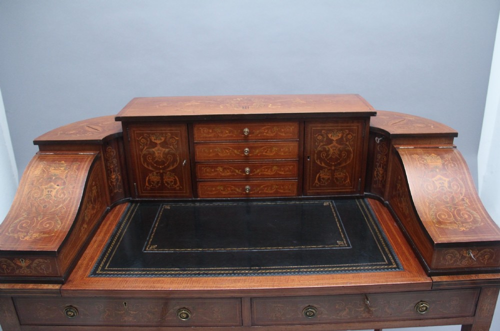 A pair of early 20th-century mahogany Carlton House desks with detailed satinwood marquetry inlay, stepped gallery drawers, and tapered legs. View XII