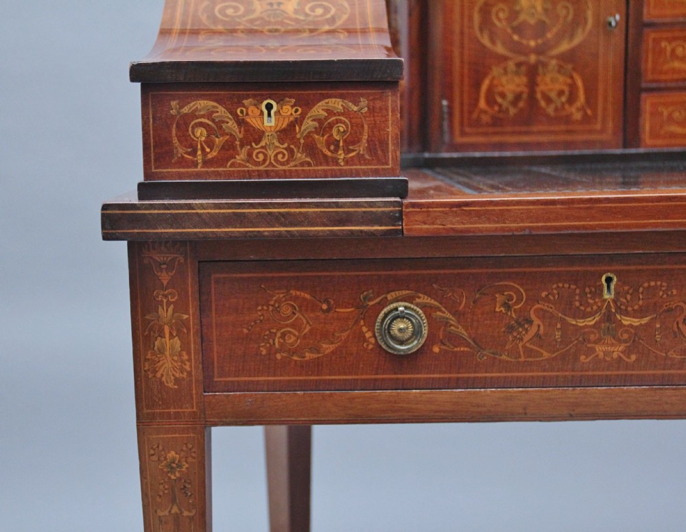 A pair of early 20th-century mahogany Carlton House desks with detailed satinwood marquetry inlay, stepped gallery drawers, and tapered legs. View XVII