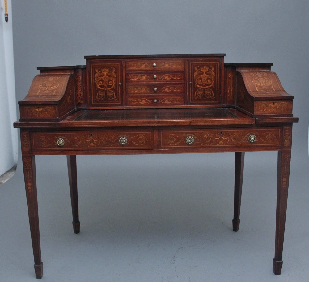 A pair of early 20th-century mahogany Carlton House desks with detailed satinwood marquetry inlay, stepped gallery drawers, and tapered legs. View XVIII