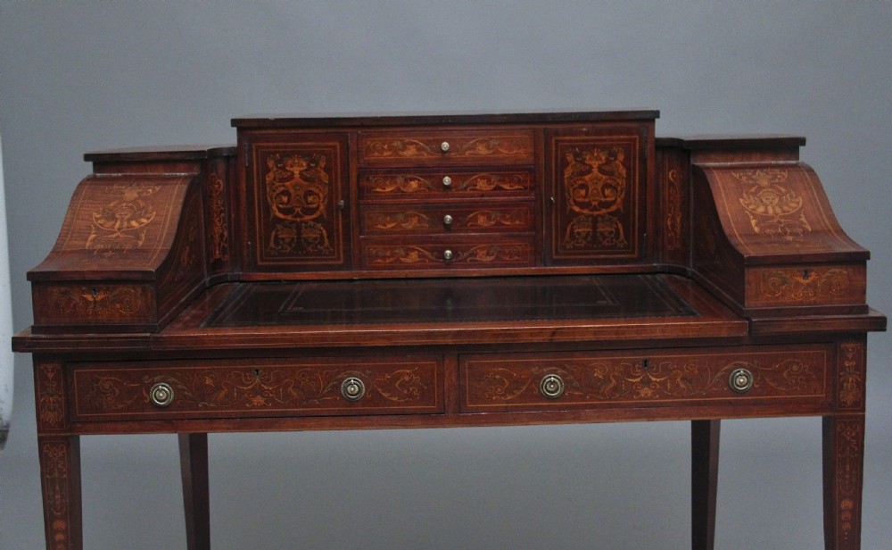 A pair of early 20th-century mahogany Carlton House desks with detailed satinwood marquetry inlay, stepped gallery drawers, and tapered legs. View XIX