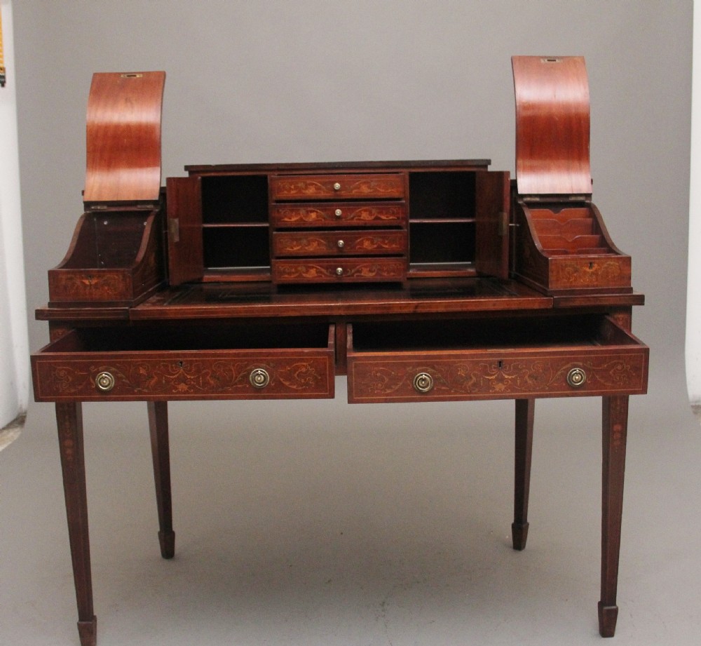 A pair of early 20th-century mahogany Carlton House desks with detailed satinwood marquetry inlay, stepped gallery drawers, and tapered legs. View XX